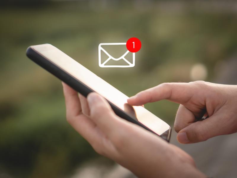 Eine Frauenhand berührt das Display eines Smartphones. Ein Icon für den Erhalt einer E-Mail ist über dem Smartphone zu sehen.